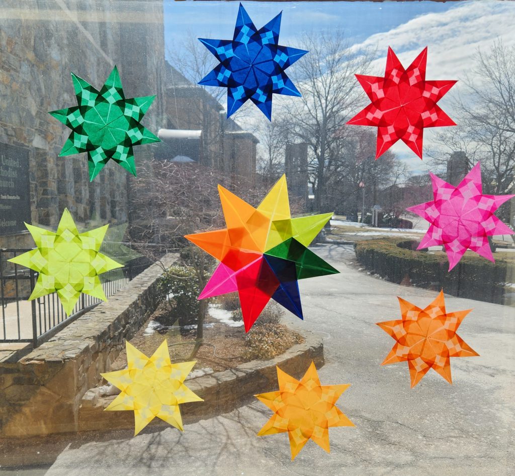 Nine colorful, translucent folded paper stars on a window.
