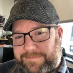 Headshot of writer-in-residence Christopher Paul Hickey, wearing a cap and eyeglasses.